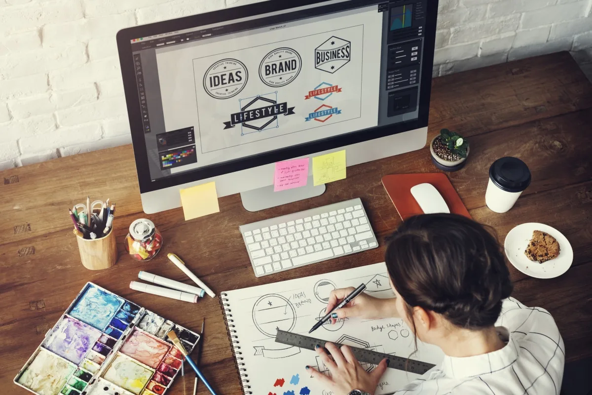 Designer sketching brand marks beside a desktop layout